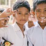 Joyful Indonesian schoolboys in white uniforms smiling and posing outdoors.