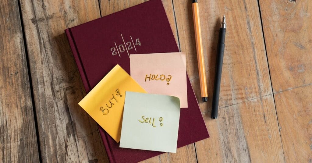 2024 planner with 'buy', 'hold', 'sell' notes and pens on a rustic wooden surface.