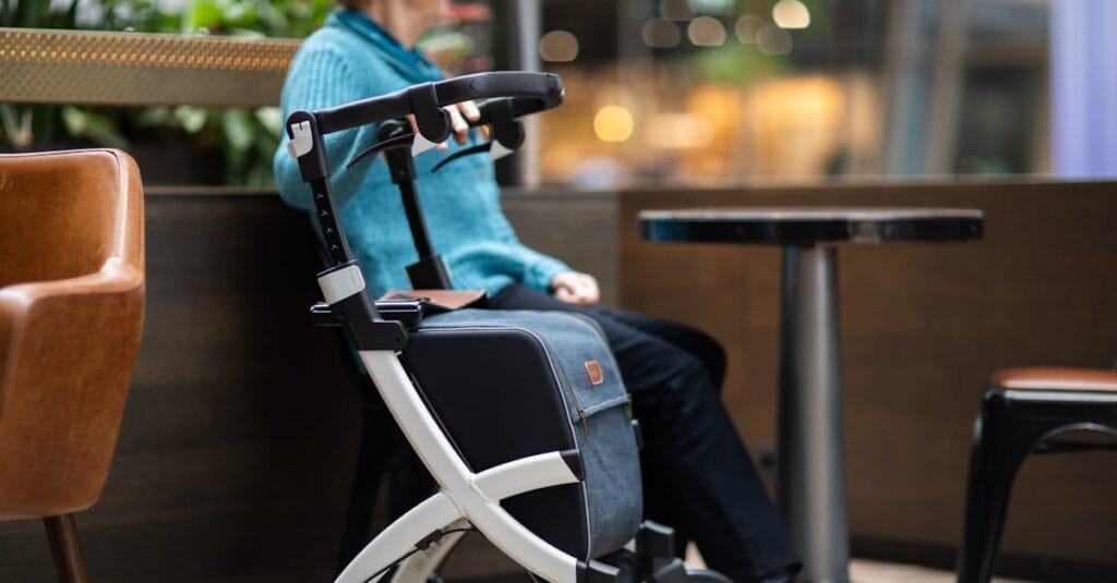 Elderly woman sits indoors in a mall with a rollator walker, enjoying leisure time.