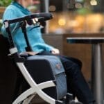 Elderly woman sits indoors in a mall with a rollator walker, enjoying leisure time.