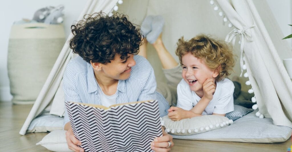 A joyful mother and son enjoying reading together in a cozy indoor tent setting.