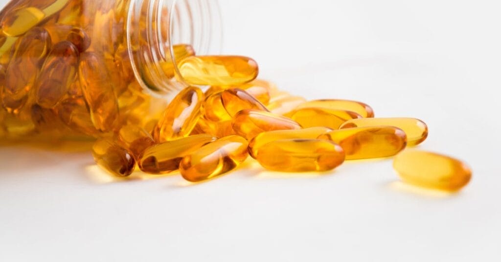 Close-up of fish oil capsules spilling from a bottle on white background.