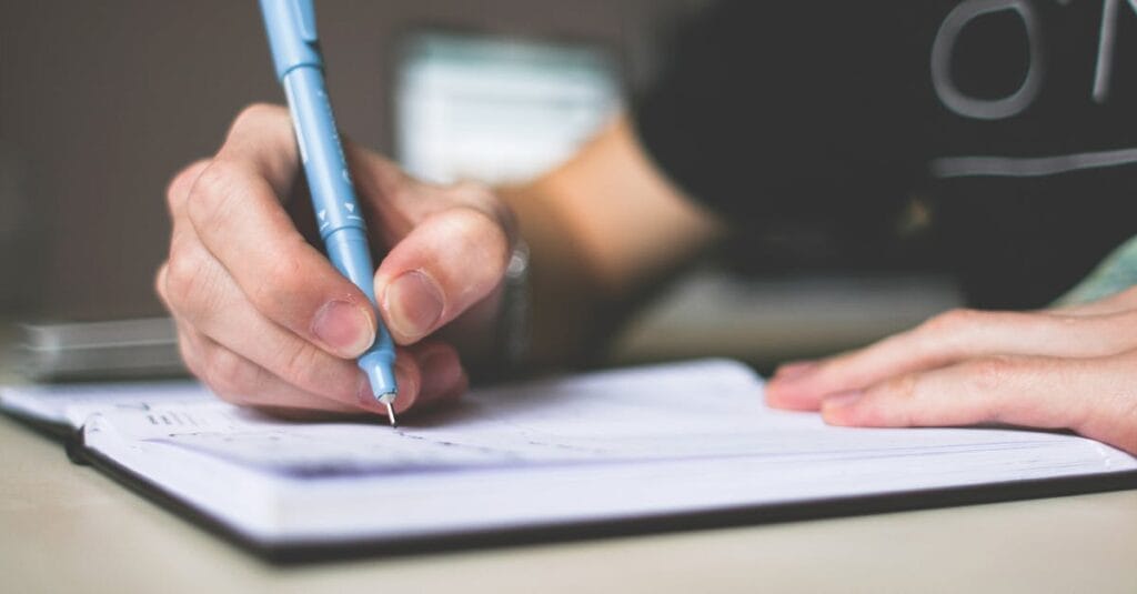 Close-up of hand writing in notebook using a blue pen, focus on creativity.