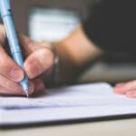 Close-up of hand writing in notebook using a blue pen, focus on creativity.