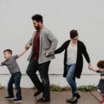 A joyful family walking together outdoors, holding hands in a playful and happy moment.