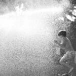 A child joyfully plays in water spray in a backyard, capturing summer fun.