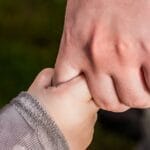 A close-up of a child and parent holding hands in a park, symbolizing love and trust.