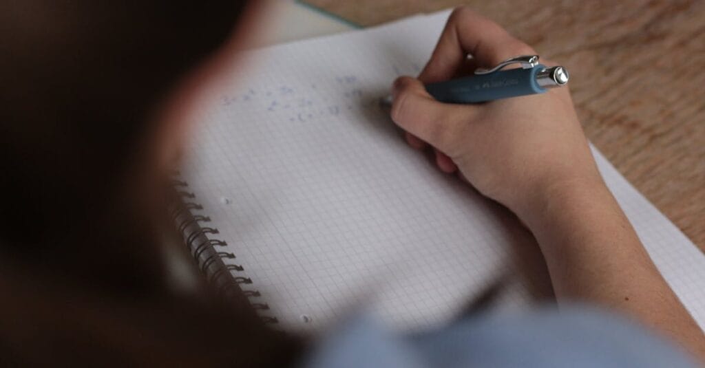 A student writes mathematical notes in a notebook using a pen, focus on studying.