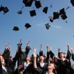 Group of graduates celebrating by throwing caps in the air during a sunny day.