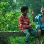 Two boys enjoying playful moments on a tree branch in a lush park setting.