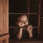 A thoughtful child rests at a window, gazing outside, conveying a moment of contemplation.