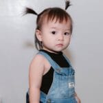 Adorable toddler with pigtails wearing a denim dress indoors.