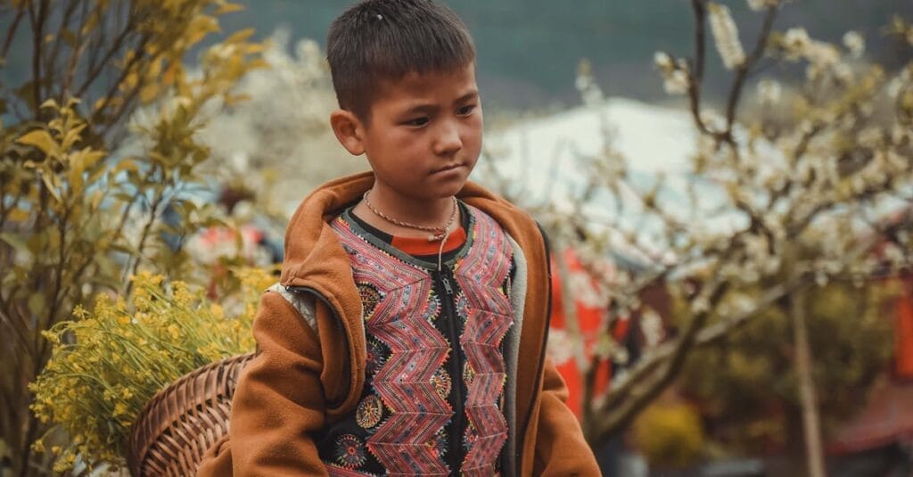 A young child in cultural attire carrying a basket in a blooming orchard during spring.