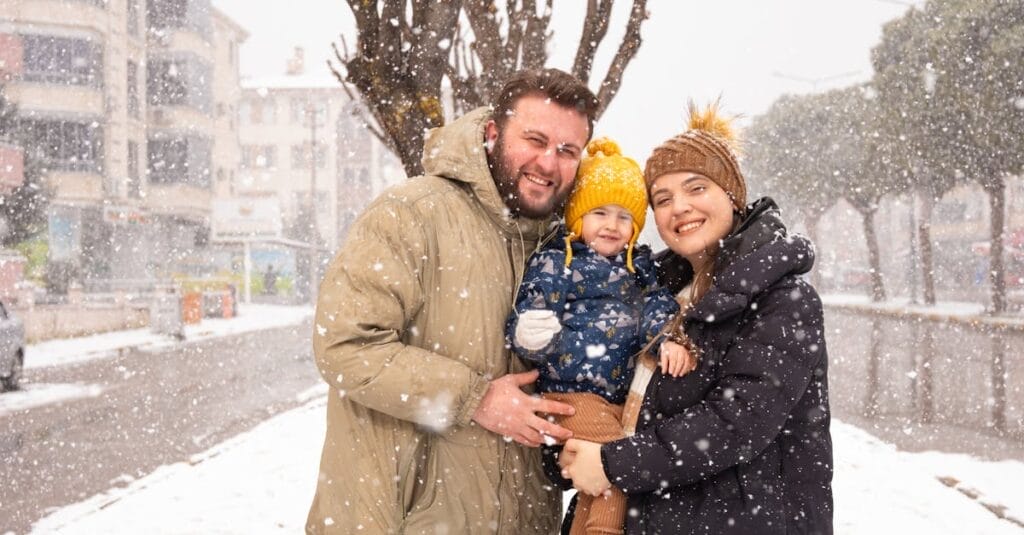 A joyful family of three embracing during a snowy day in winter.