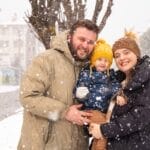 A joyful family of three embracing during a snowy day in winter.