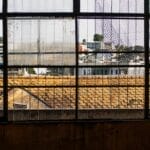 A child gazes outside through a large window, revealing an urban landscape with buildings in the background.