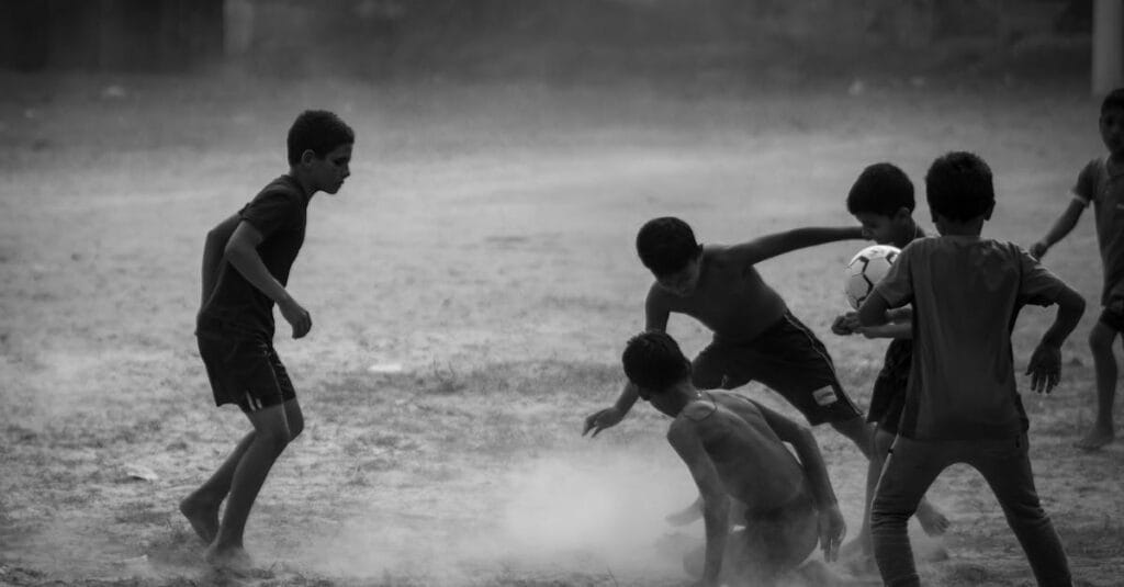 Children engaged in an energetic football game on a dusty outdoor field.