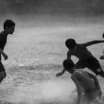 Children engaged in an energetic football game on a dusty outdoor field.