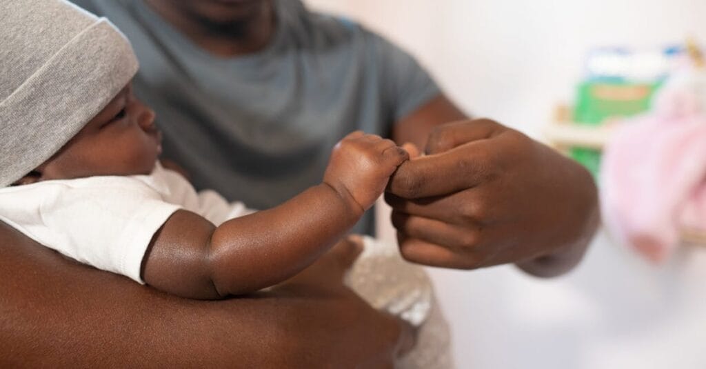 Heartwarming scene of a father gently holding his infant's hand indoors.