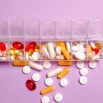 A daily pill organizer filled with various pills and capsules on a purple background. Ideal for healthcare topics.