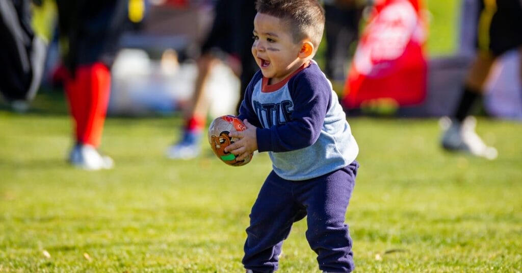 Joyful toddler playing with a football on a sunny day outdoors, dressed in casual clothes.