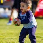 Joyful toddler playing with a football on a sunny day outdoors, dressed in casual clothes.