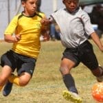 Two young boys energetically competing in a soccer match on a grassy field.