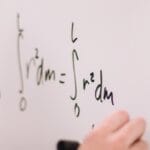 Person writing math equations on a whiteboard, focusing on integrals and formulas.