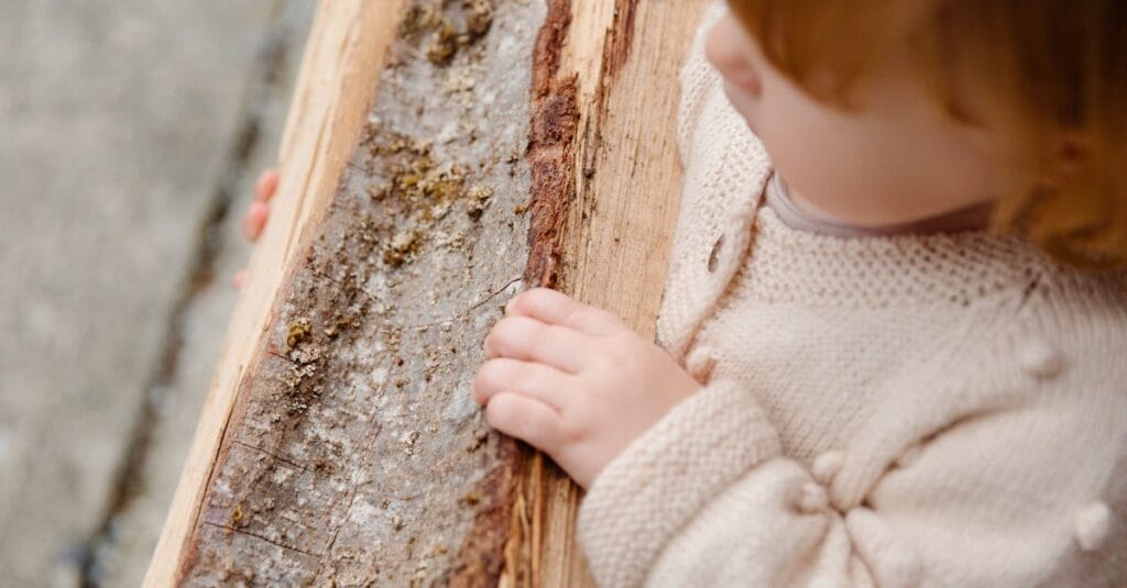 From above of little girl standing with firewood looking away and thinking while spending time in countryside during weekend and enjoying