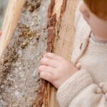 From above of little girl standing with firewood looking away and thinking while spending time in countryside during weekend and enjoying