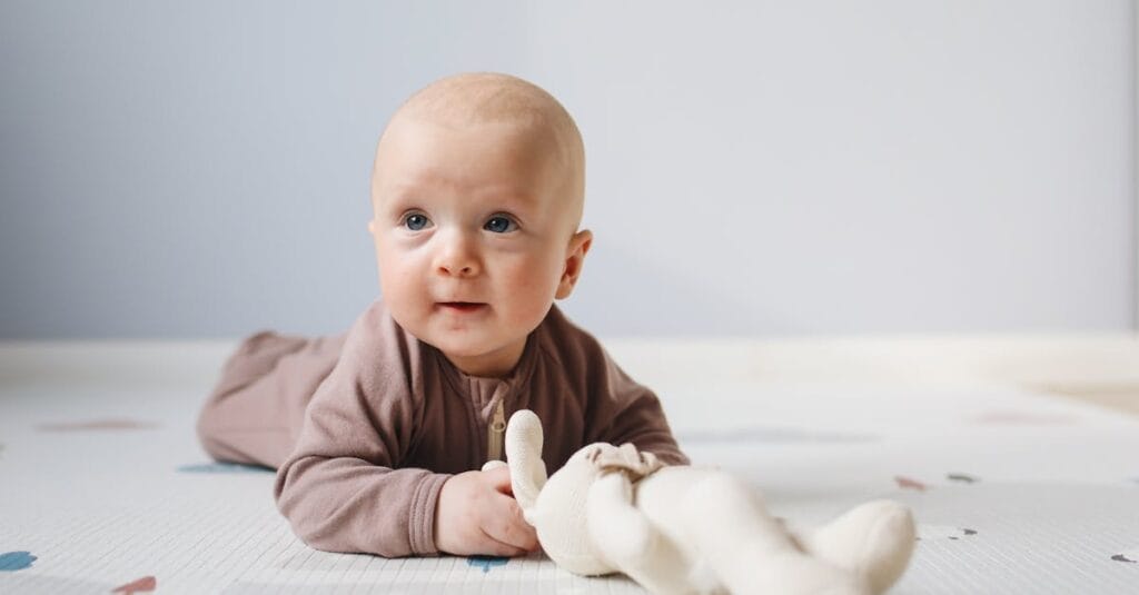 Cute baby on floor with stuffed toy, light indoor setting, focus on facial expression.