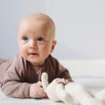 Cute baby on floor with stuffed toy, light indoor setting, focus on facial expression.