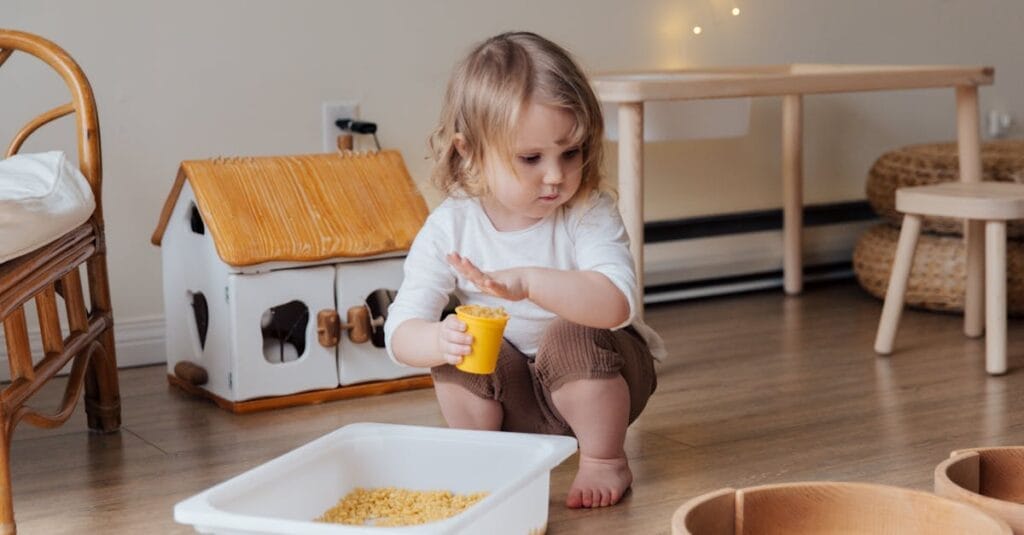 A young child playing with macaroni in a cozy indoor playroom setting.