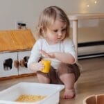 A young child playing with macaroni in a cozy indoor playroom setting.