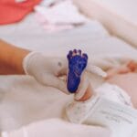 Medical professional taking footprint of a newborn baby in hospital setting.