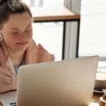 Young woman with Down syndrome using a laptop at home, enjoying coffee. Perfect for lifestyle and technology themes.