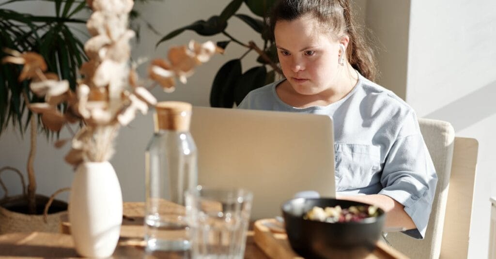 Young woman with Down syndrome using a laptop at a cozy home setting, enjoying leisure time.