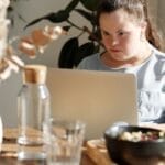 Young woman with Down syndrome using a laptop at a cozy home setting, enjoying leisure time.