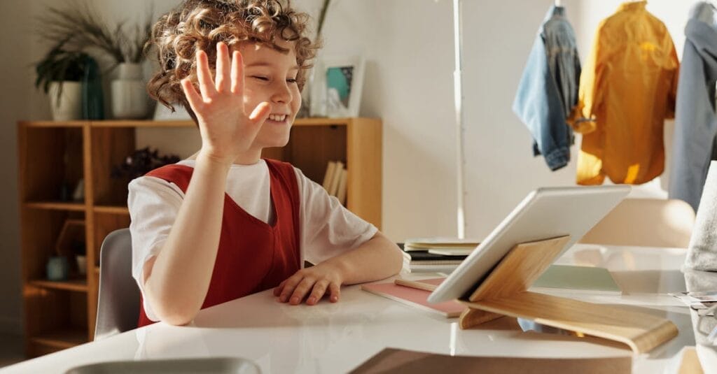 Happy child waving during an online learning session at home.