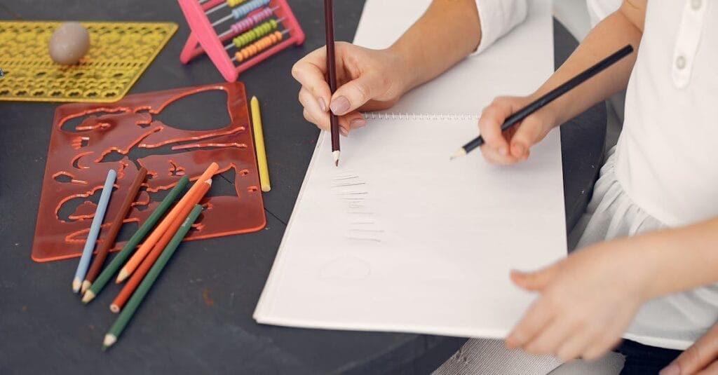 A mother and child drawing together at a table, emphasizing early education and creativity.
