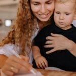 Mother holding her young child while writing, creating a bonding moment indoors.