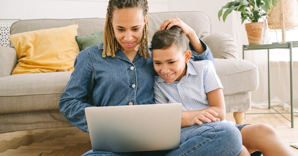 A loving mother and her son enjoying a fun time together while using a laptop indoors.