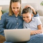 A loving mother and her son enjoying a fun time together while using a laptop indoors.