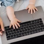 Top view of a parent and a child's hands on a laptop keyboard, symbolizing digital learning.