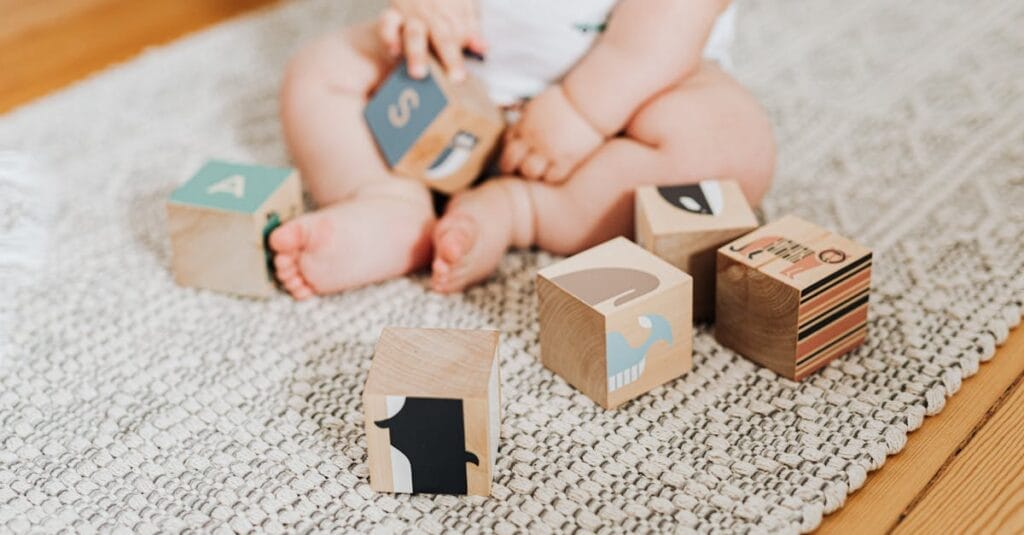 Adorable baby sitting on a rug and playing with colorful wooden blocks.