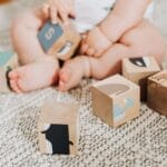 Adorable baby sitting on a rug and playing with colorful wooden blocks.