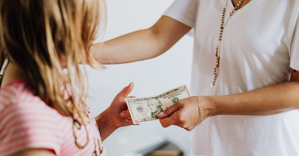 A woman handing money to a young girl, symbolizing family financial education and transactions.