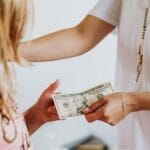 A woman handing money to a young girl, symbolizing family financial education and transactions.