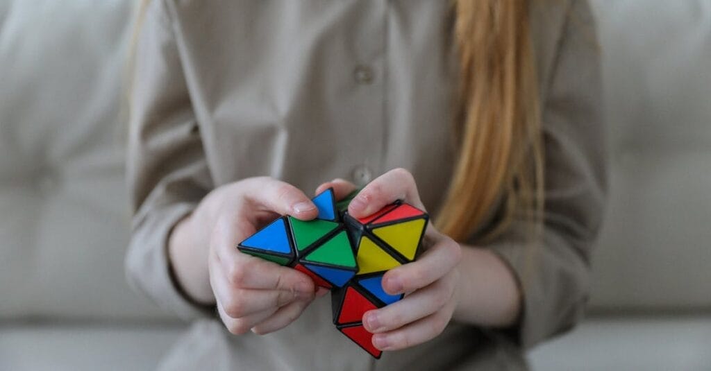 Crop anonymous girl demonstrating and solving colorful puzzle with triangles in soft focus