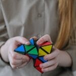 Crop anonymous girl demonstrating and solving colorful puzzle with triangles in soft focus